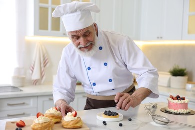 Photo of Elderly pastry chef making desserts at table in kitchen