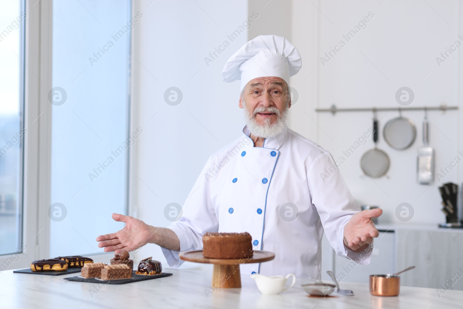 Photo of Elderly pastry chef at table with desserts in kitchen