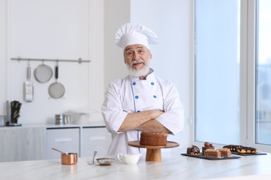 Photo of Elderly pastry chef at table with desserts in kitchen