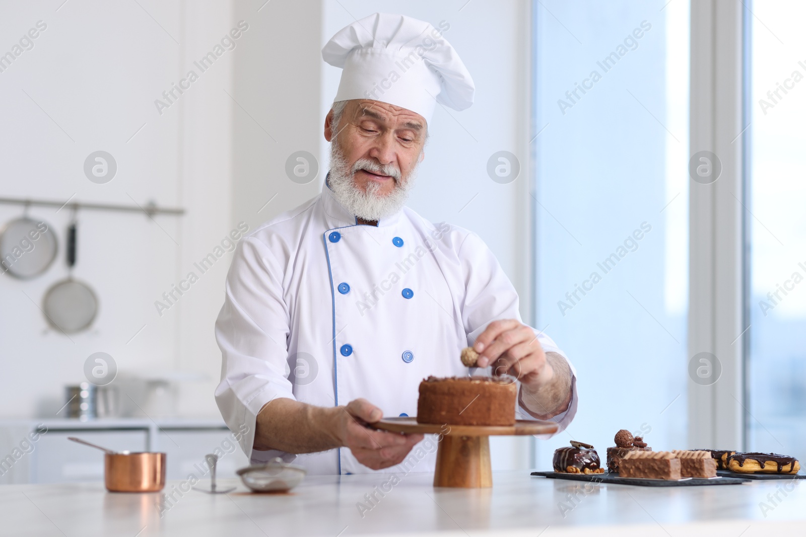 Photo of Elderly pastry chef decorating tasty cake at table in kitchen