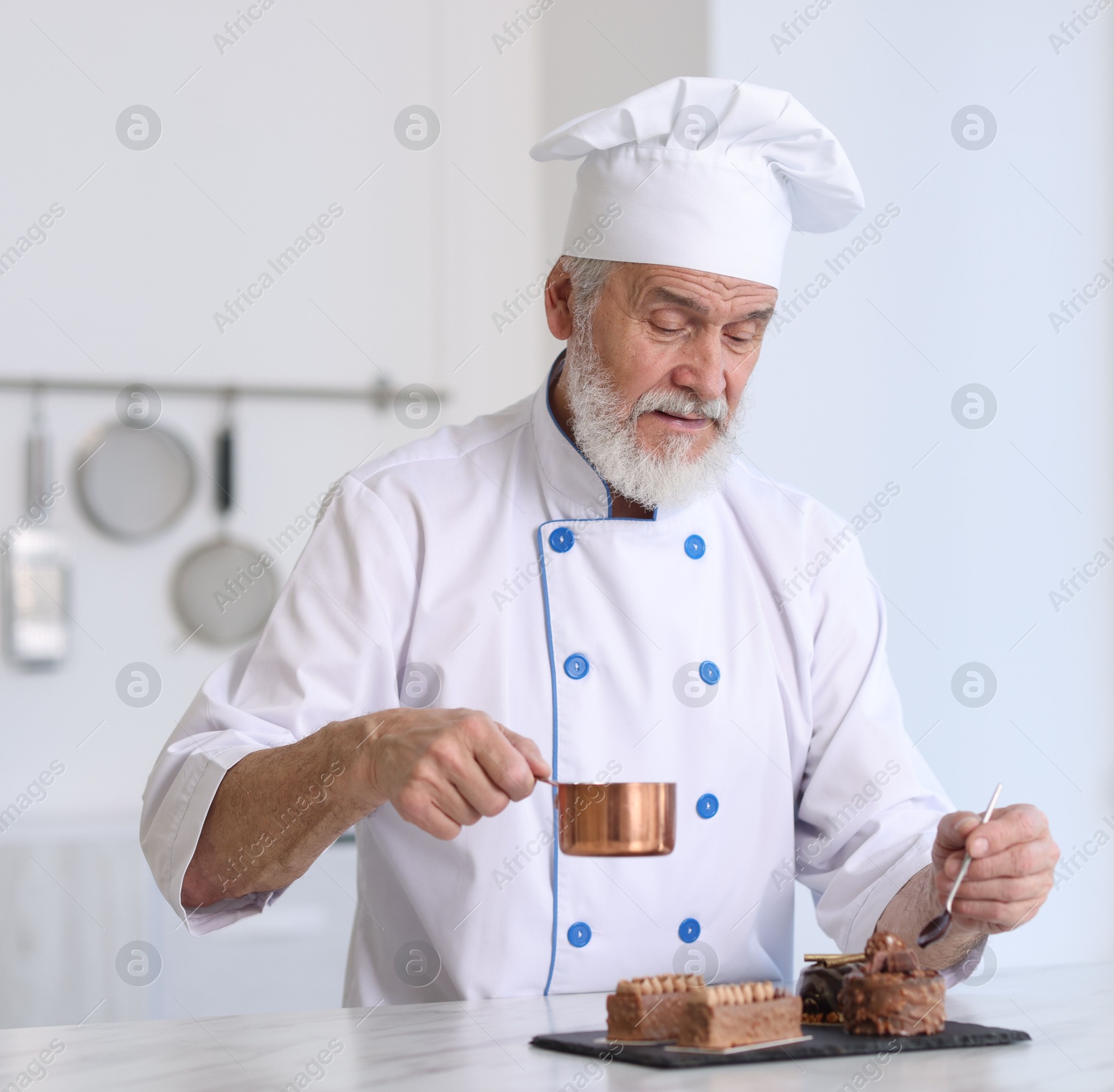 Photo of Elderly pastry chef decorating tasty desserts with melted chocolate at table in kitchen