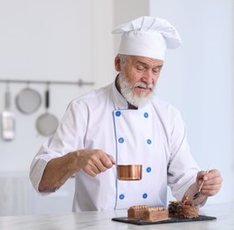 Elderly pastry chef decorating tasty desserts with melted chocolate at table in kitchen