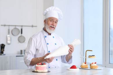 Elderly confectioner with pastry bag making cake at table in kitchen