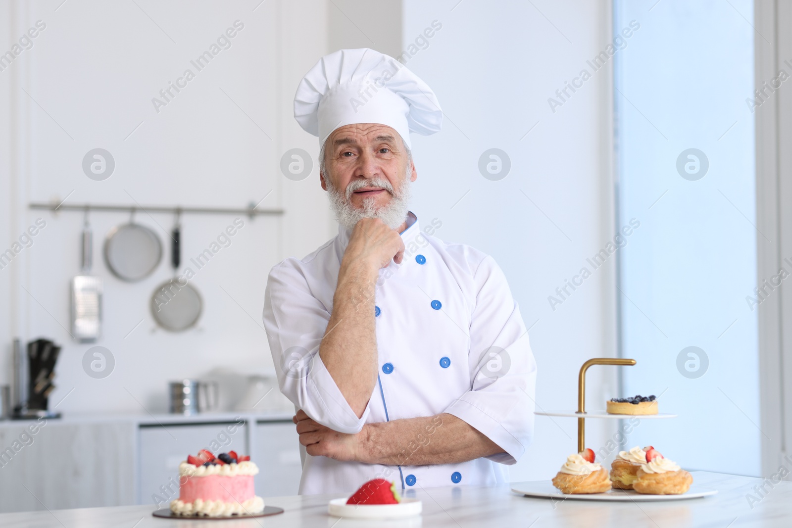 Photo of Elderly pastry chef at table with desserts in kitchen