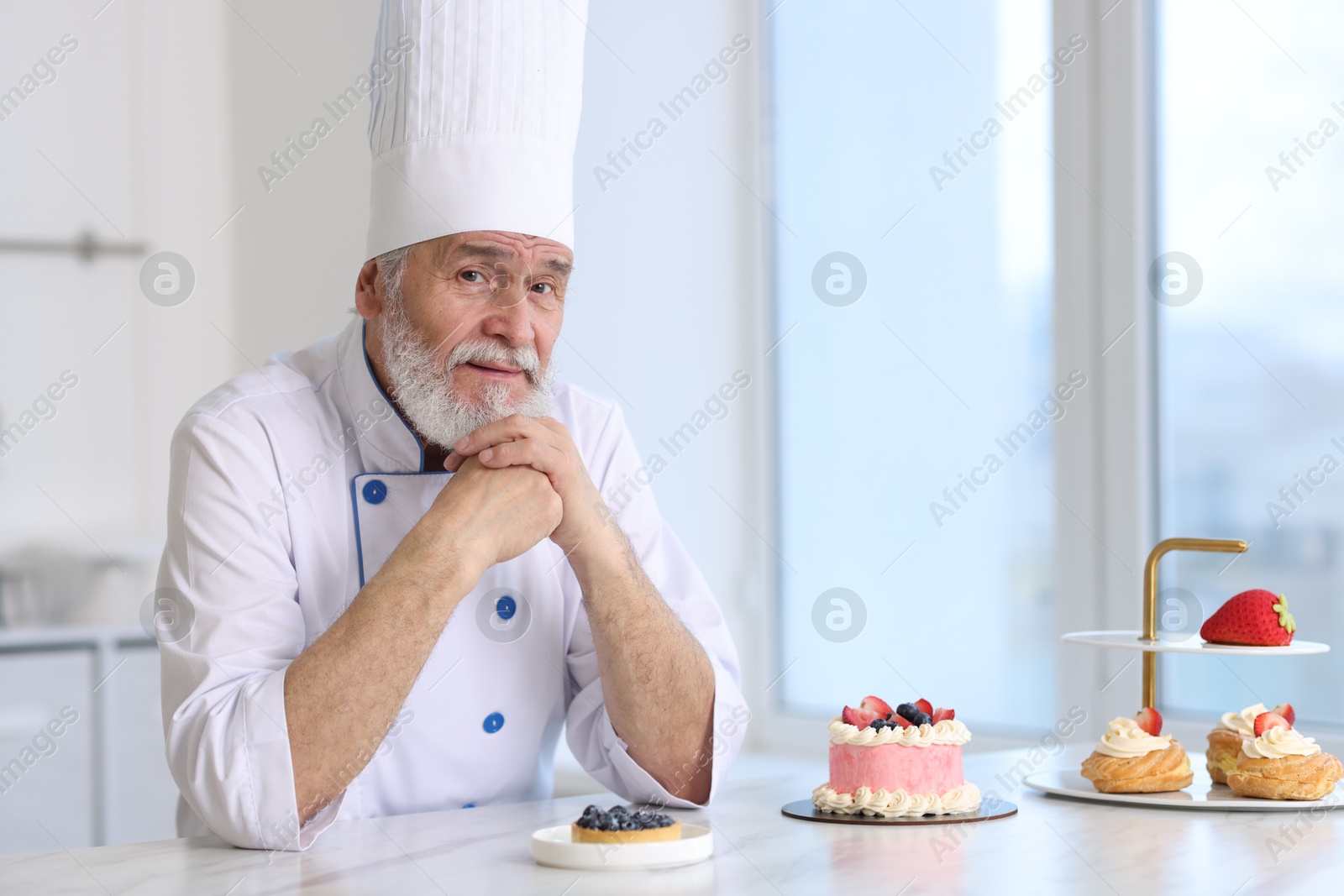 Photo of Elderly pastry chef at table with desserts in kitchen