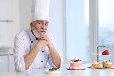 Photo of Elderly pastry chef at table with desserts in kitchen