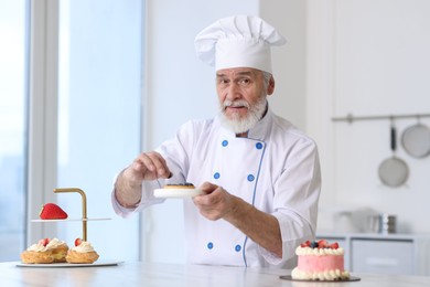 Photo of Elderly pastry chef making dessert at table in kitchen