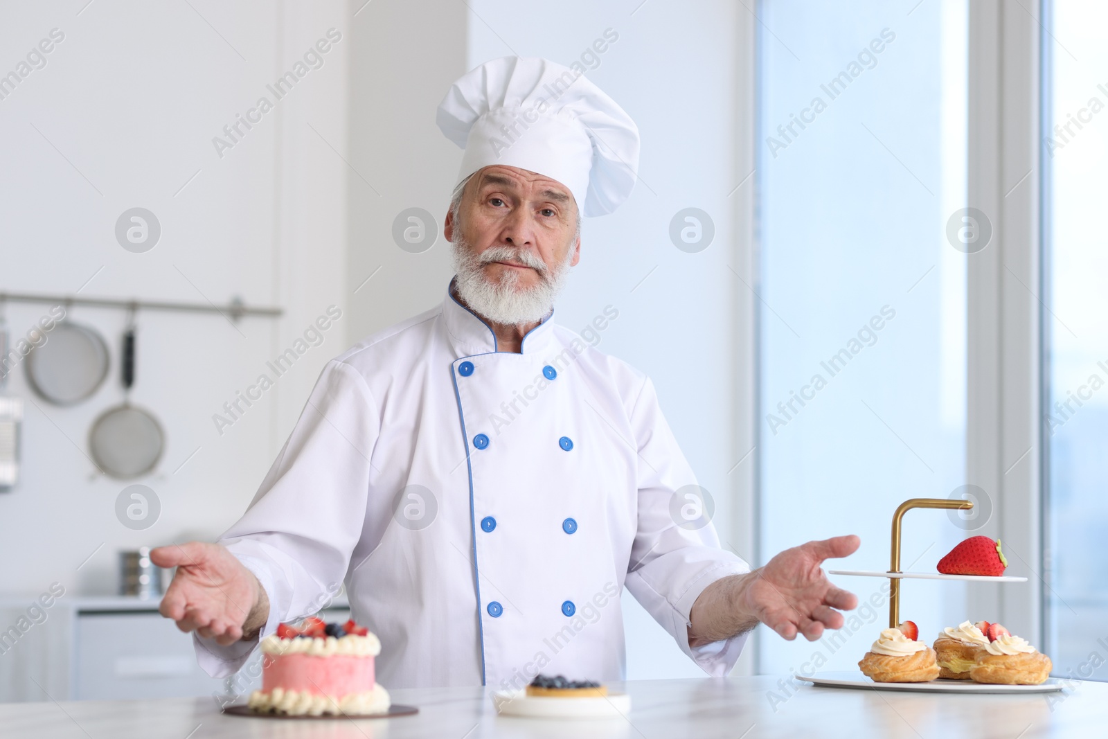 Photo of Elderly pastry chef at table with desserts in kitchen