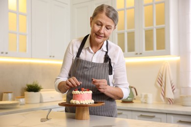 Smiling pastry chef decorating cake with berries at table in kitchen