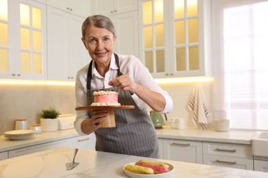 Smiling pastry chef decorating cake with berries at table in kitchen