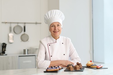 Photo of Smiling pastry chef at table with desserts in kitchen