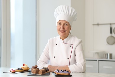 Smiling pastry chef at table with desserts in kitchen