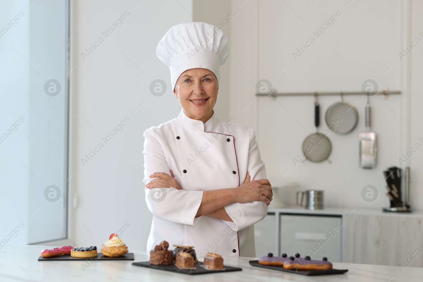 Photo of Smiling pastry chef at table with desserts in kitchen