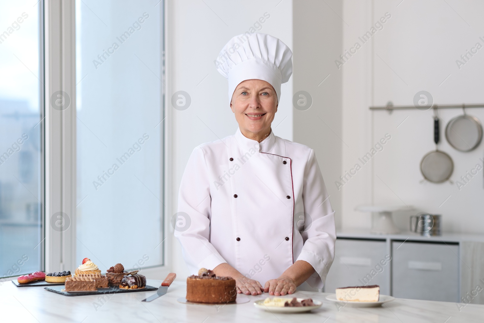 Photo of Smiling pastry chef at table with desserts in kitchen