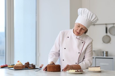 Senior pastry chef at table with desserts in kitchen. Space for text