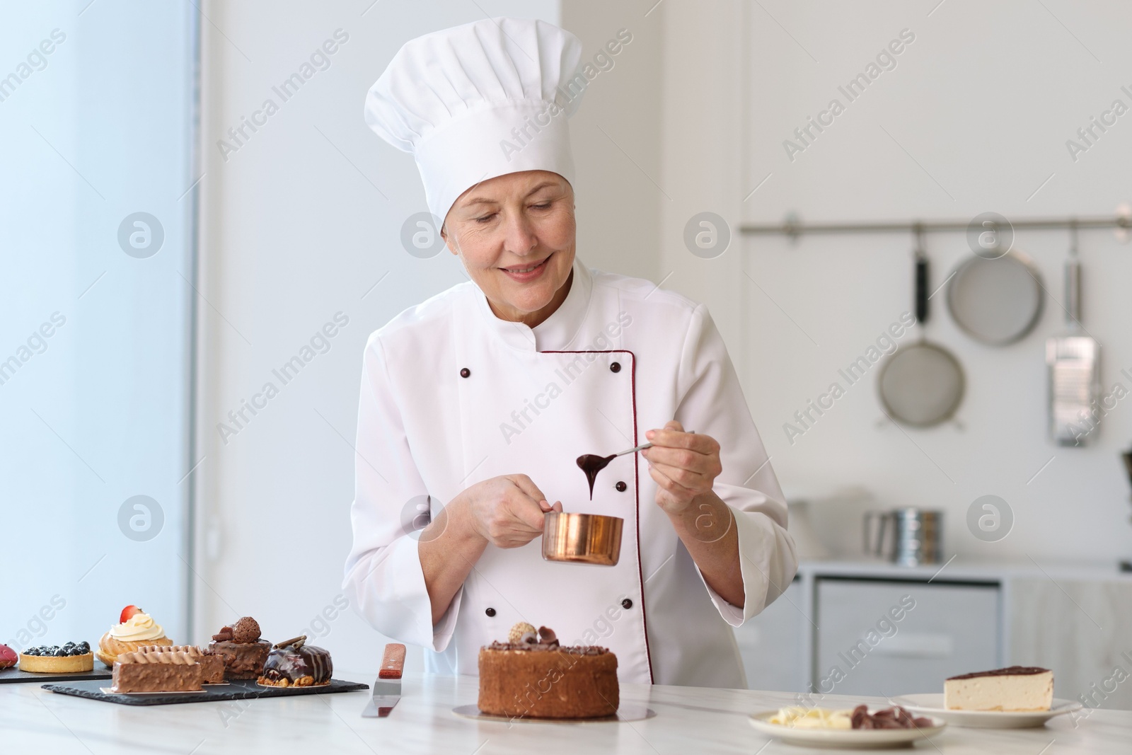 Photo of Smiling pastry chef decorating cake with melted chocolate at table in kitchen