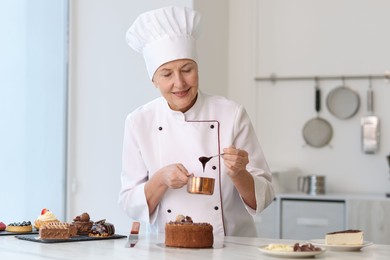 Smiling pastry chef decorating cake with melted chocolate at table in kitchen