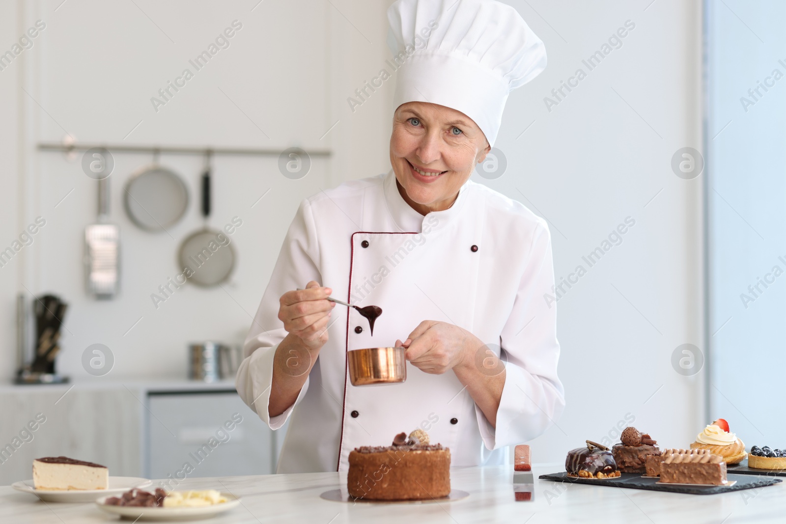 Photo of Smiling pastry chef decorating cake with melted chocolate at table in kitchen