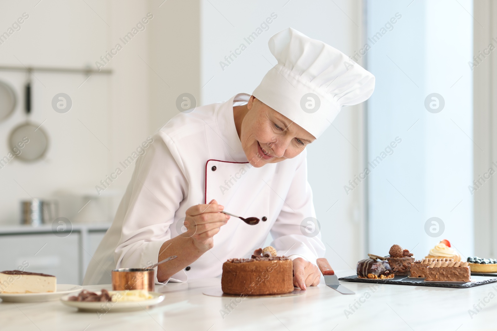 Photo of Senior pastry chef decorating cake with melted chocolate at table in kitchen