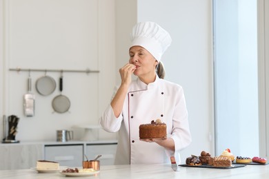 Senior pastry chef holding tasty cake at table with other desserts in kitchen