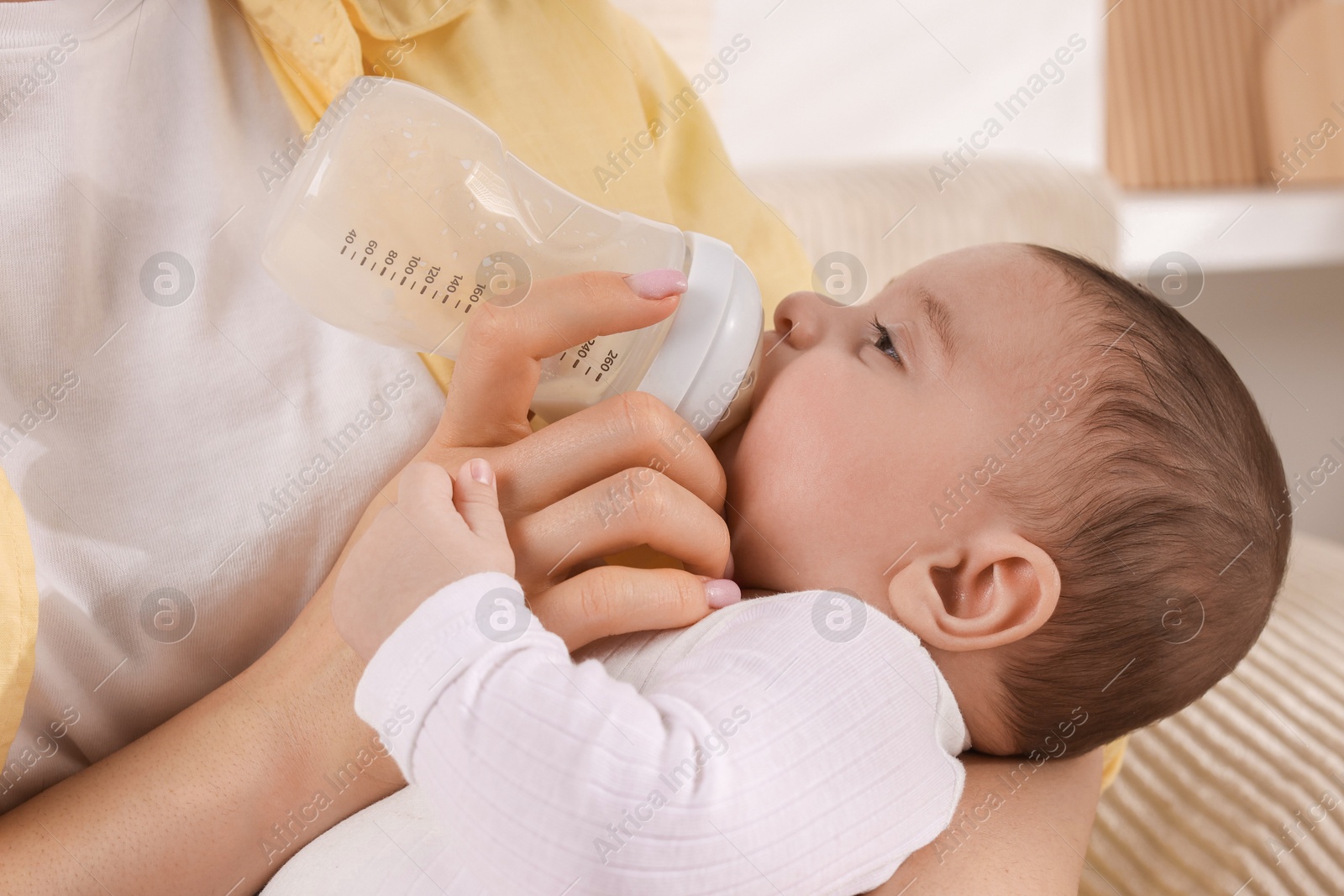 Photo of Mother feeding her little baby from bottle indoors, closeup