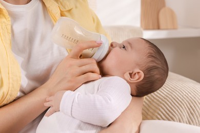 Photo of Mother feeding her little baby from bottle indoors, closeup