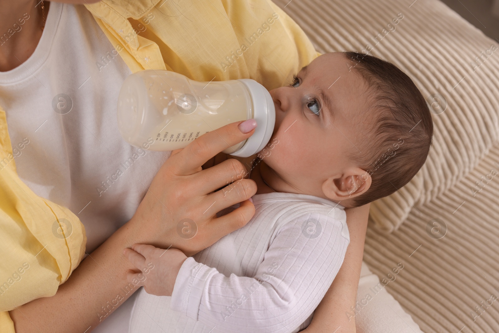 Photo of Mother feeding her little baby from bottle indoors, closeup