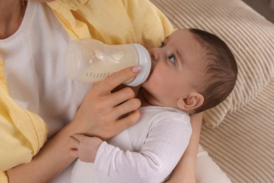 Photo of Mother feeding her little baby from bottle indoors, closeup