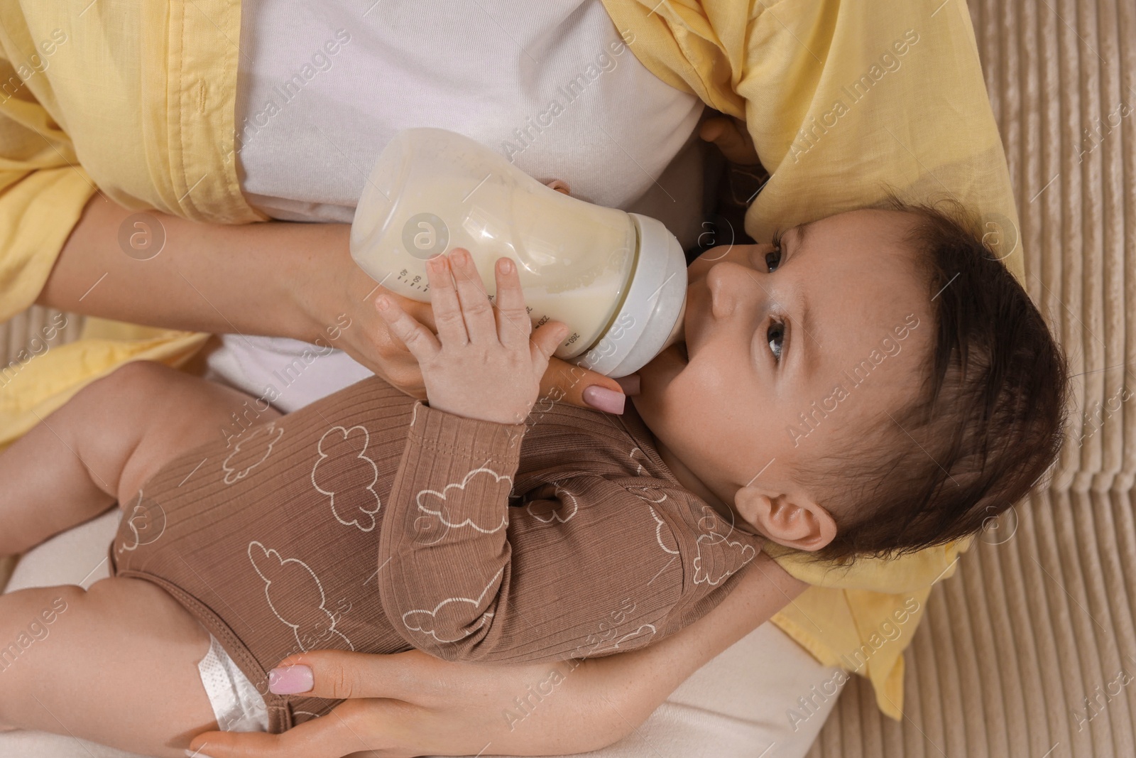 Photo of Mother feeding her little baby from bottle indoors, closeup