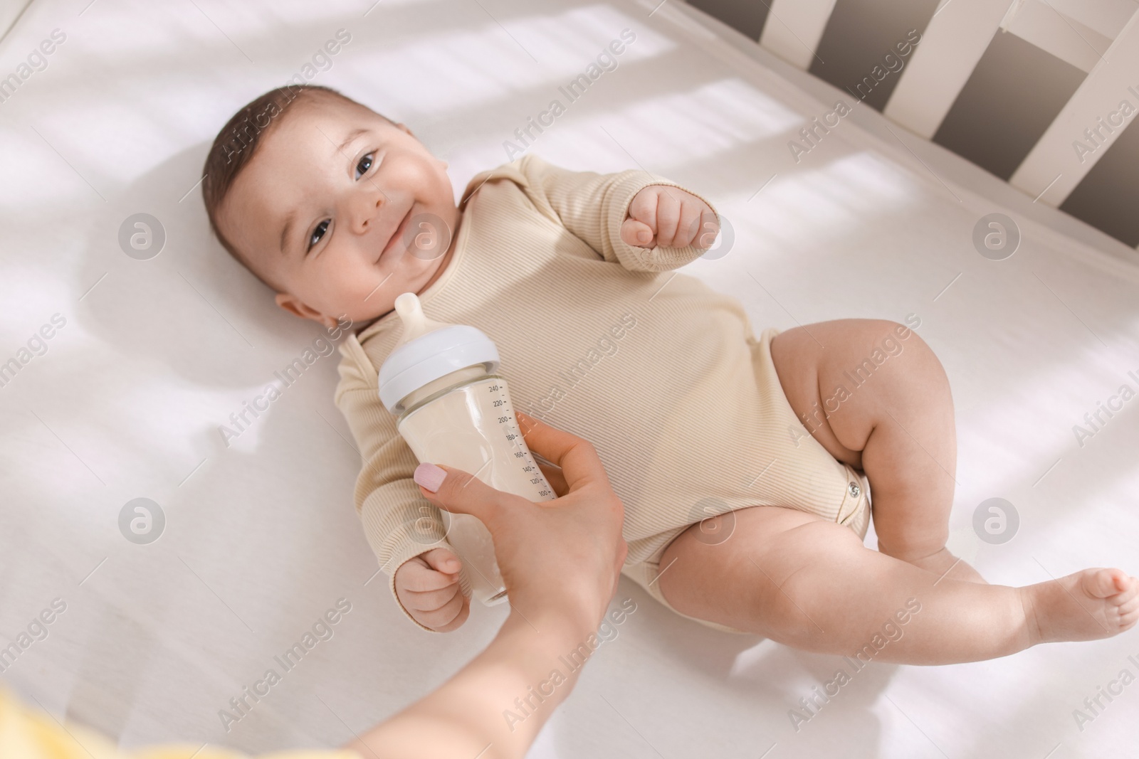 Photo of Mother feeding her little baby from bottle indoors, top view