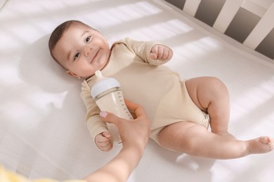 Photo of Mother feeding her little baby from bottle indoors, top view