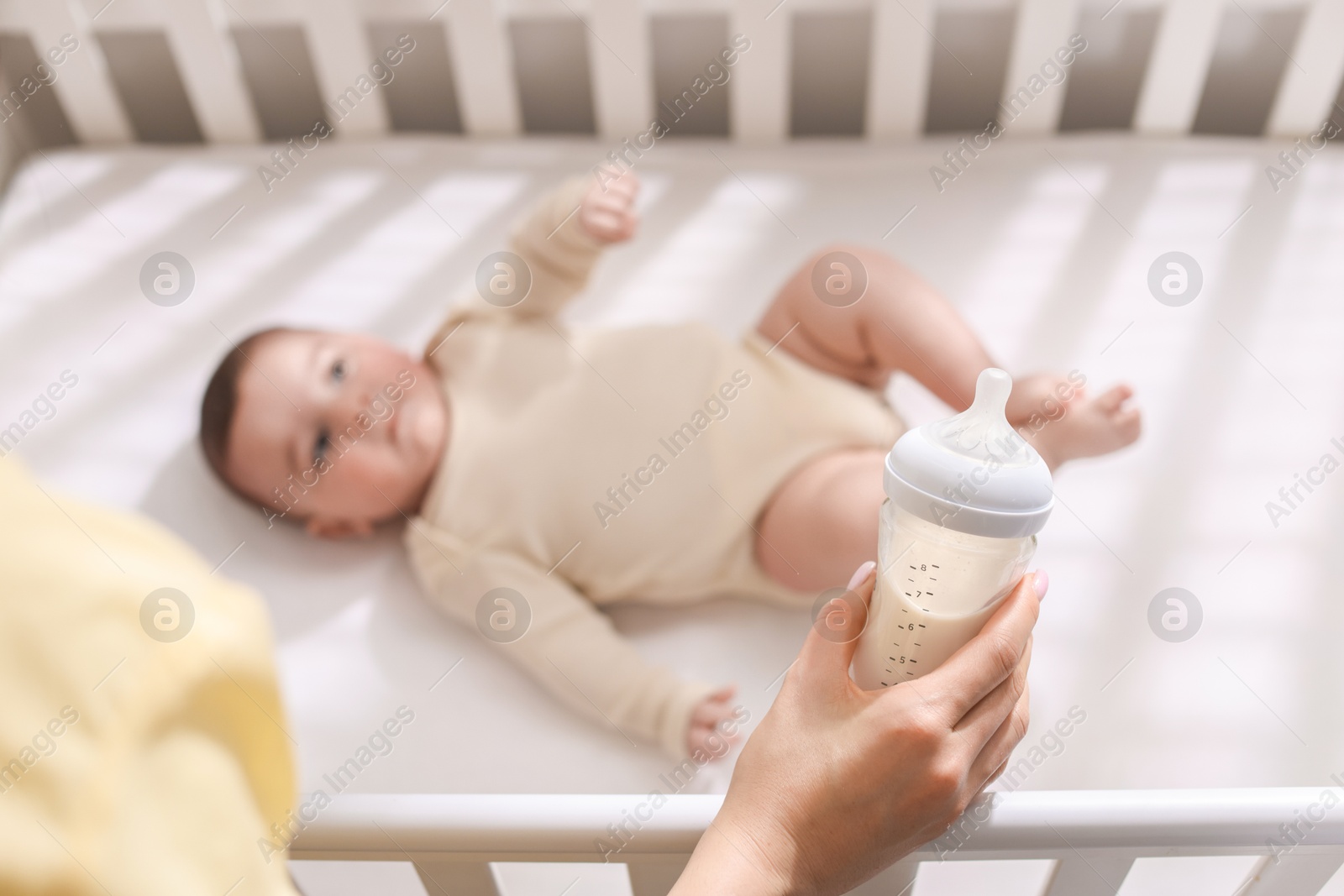 Photo of Mother with feeding bottle of milk near her little baby indoors, above view