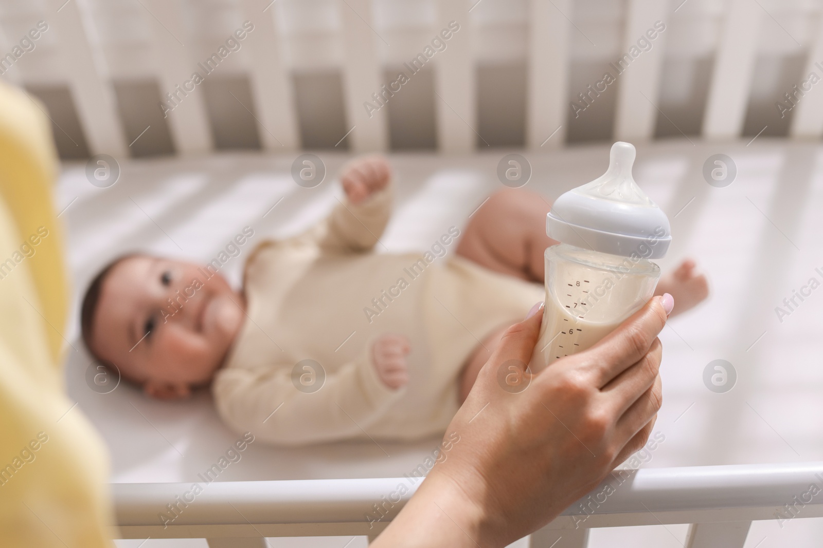 Photo of Mother with feeding bottle of milk near her little baby indoors, selective focus