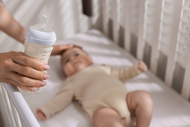 Photo of Mother with feeding bottle of milk near her little baby indoors, selective focus