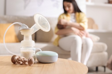 Mother holding her little baby indoors, focus on breast pump, teether and feeding bottle with milk