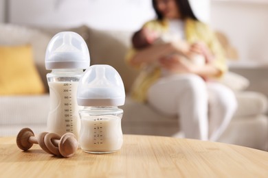 Photo of Mother holding her little baby indoors, focus on feeding bottles with milk and teether