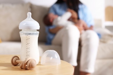 Photo of Mother holding her little baby indoors, focus on feeding bottle with milk and teether