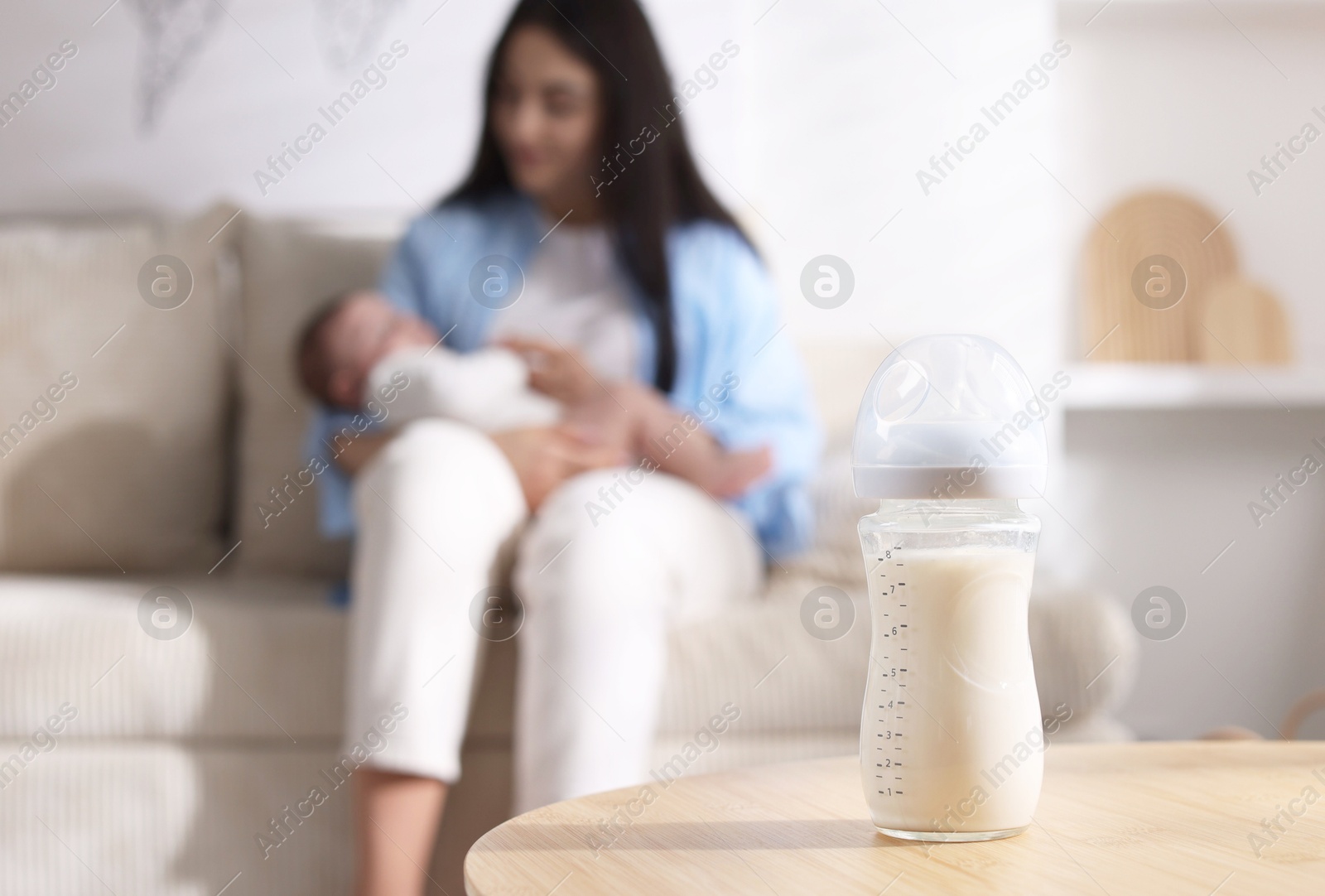 Photo of Mother holding her little baby indoors, focus on feeding bottle with milk