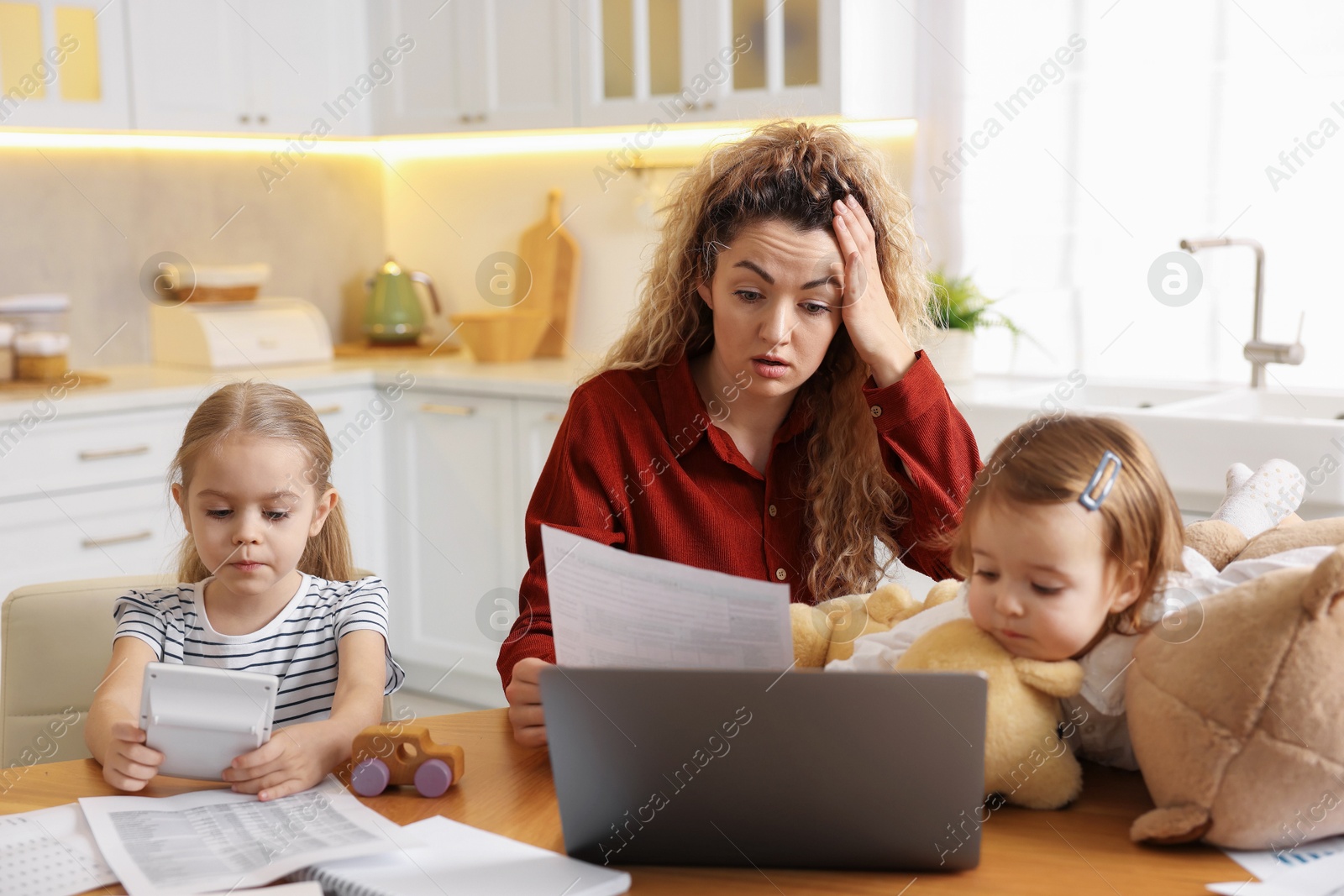 Photo of Work-family balance. Single mother with document and her daughters at table in kitchen