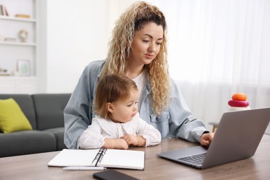 Photo of Single mother working with laptop and her daughter at table indoors