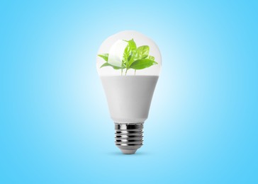 Image of Light bulb with fresh leaves inside on light blue background. Concepts of eco-friendly environment and saving energy