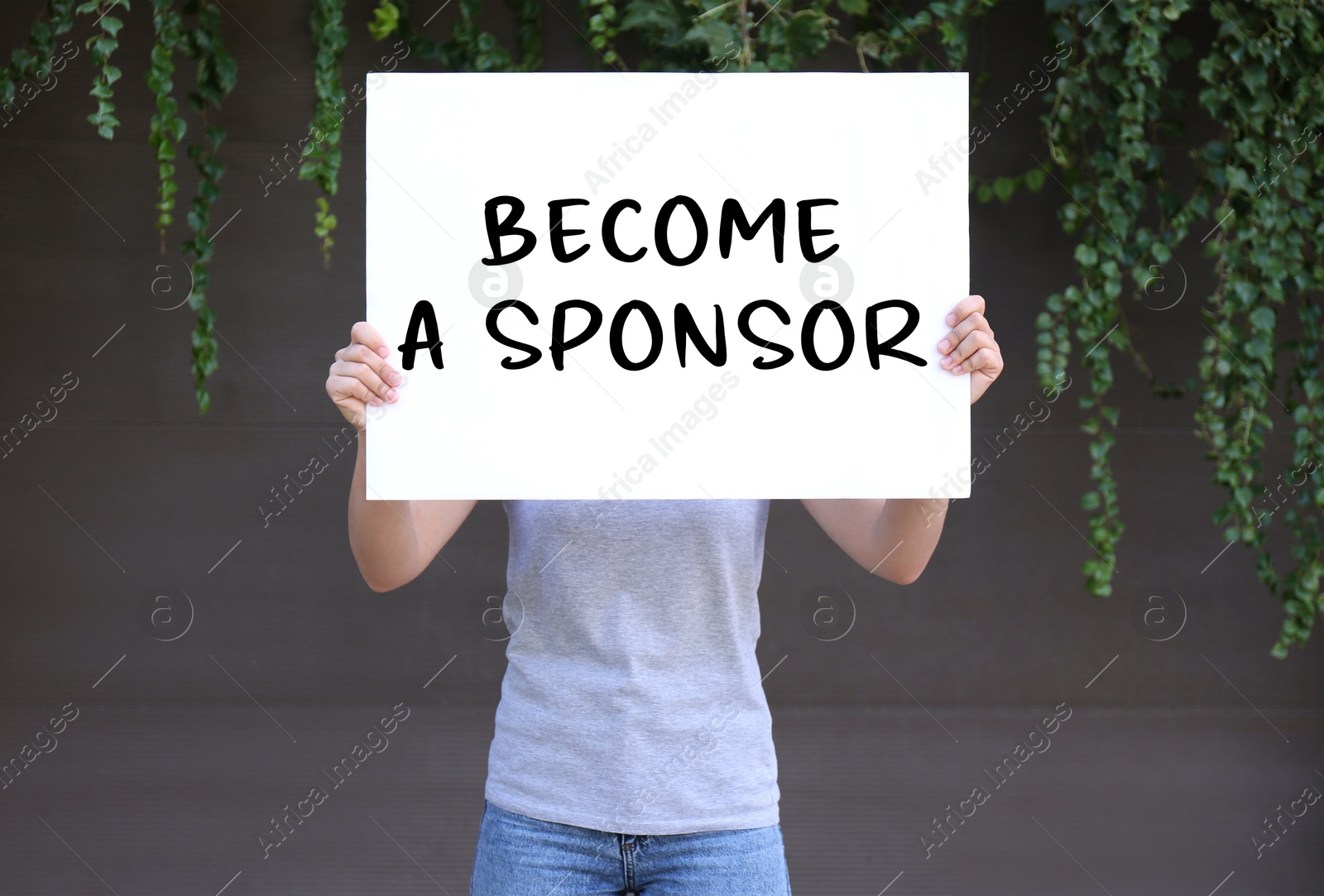 Image of Woman holding white poster with text Become A Sponsor outdoors, closeup