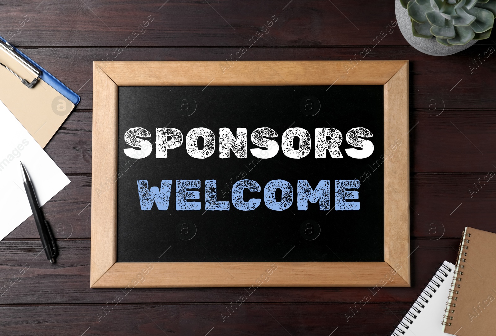 Image of Small chalkboard with text Sponsors Welcome, plant and stationery on wooden table, flat lay