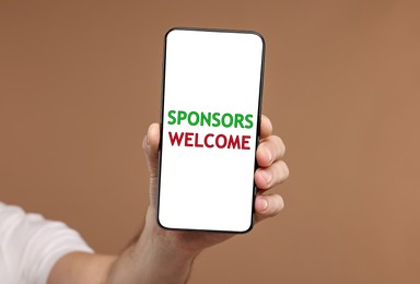 Image of Man showing smartphone with text Sponsors Welcome on screen against pale brown background, closeup