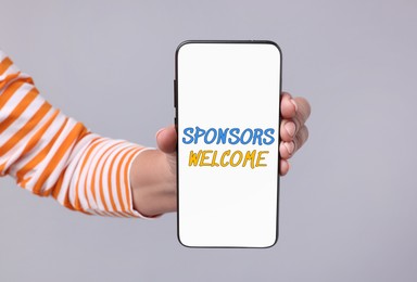 Woman showing smartphone with text Sponsors Welcome on screen against light grey background, closeup