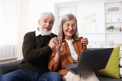 Happy elderly couple having video call by laptop on sofa at home