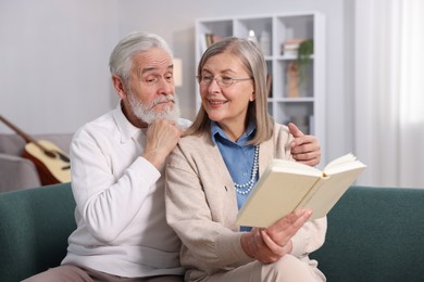 Photo of Happy elderly couple reading book together on sofa at home