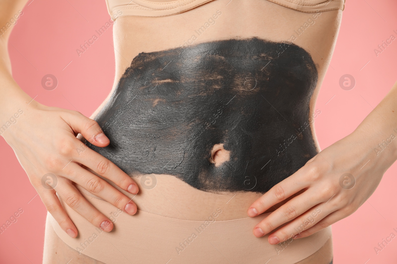 Photo of Woman doing spa body wraps on her belly against pink background, closeup