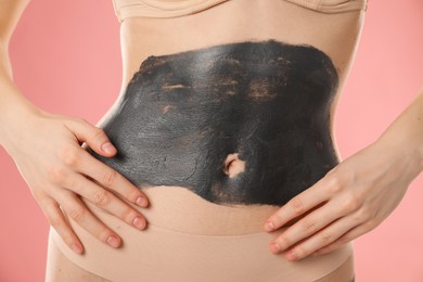 Woman doing spa body wraps on her belly against pink background, closeup