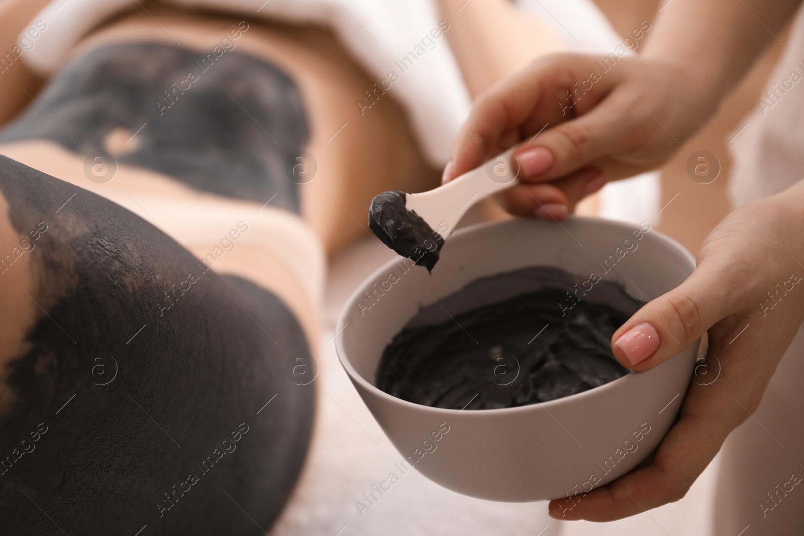 Photo of Esthetician applying cosmetic product for body wraps treatment onto woman's leg in spa salon, closeup